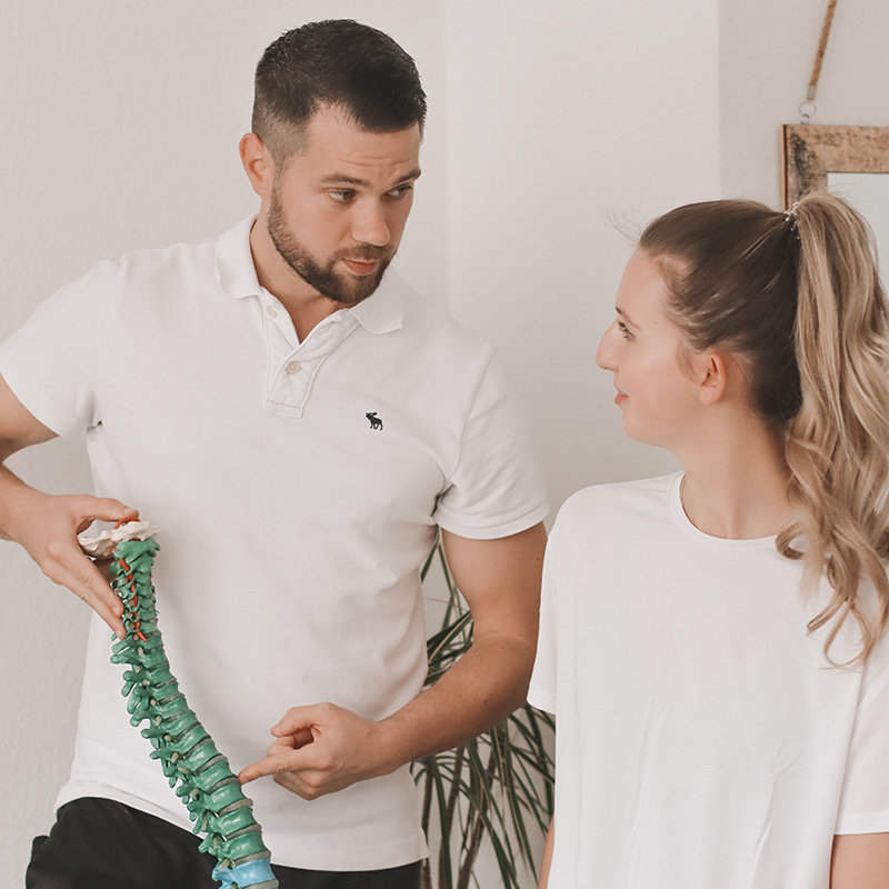 Physiotherapeut erklärt Patientin anhand eines Wirbelsäulenmodells den Rückenaufbau